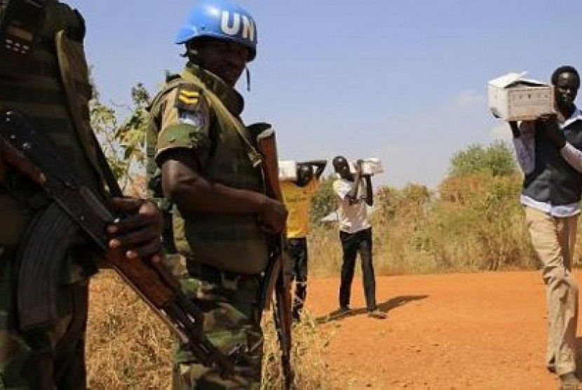 Sejumlah pria membawa kotak berjalan melintas di depan personel Pasukan PBB Sudan Selatan yang menjaga pengungsi akibat pertempuran terkini. AS menempatkan 150 Marinir ke Afrika untuk memudahkan proses evakuasi bila dibutuhkan sewaktu-waktu.
