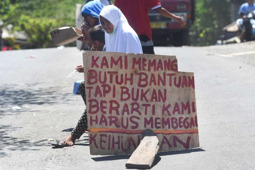 Sejumlah remaja pengungsi korban gempa bumi meminta bantuan di tengah jalan di sekitar lokasi tempat pengungsian darurat di Kayangan, Lombok Utara, NTB, Minggu (12/8). 