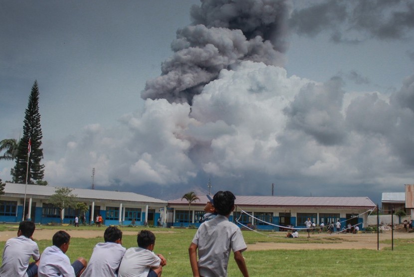 Sejumlah siswa bermain di halaman sekolah dengan latar belakang Gunung Sinabung yang mengeluarkan material vulkanik, di desa Ndokum Siroga, Karo, Sumatera Utara, Selasa (11/4).