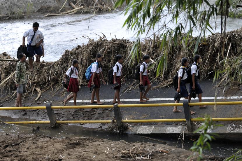 Sejumlah siswa dan warga berjalan di jembatan beton yang ambruk saat berangkat ke sekolah pascabanjir bandang di Dusun Sekar Kejula Kelod, Desa Yehembang Kauh, Jembrana, Bali, Selasa (25/10/2022). Sejak jembatan beton penghubung empat dusun yakni Dusun Sekar Kejula Kelod, Dusun Sekar Kejula, Dusun Kedisan, dan Dusun Munduk Anggrek tersebut ambruk akibat diterjang banjir bandang yang terjadi pada Minggu (16/10) lalu, banyak siswa dan warga memilih menyeberang sungai dengan berjalan kaki saat menuju sekolah maupun kantor desa menyusul jauhnya jarak jalur alternatif di dusun itu. 