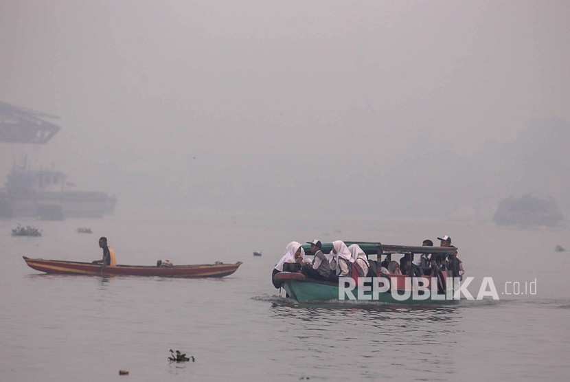 Sejumlah siswa menaiki kapal motor menembus kabut asap akibat kebakaran lahan di Sungai Ogan, Palembang, Sumatera Selatan, Senin (16/9/2019). 