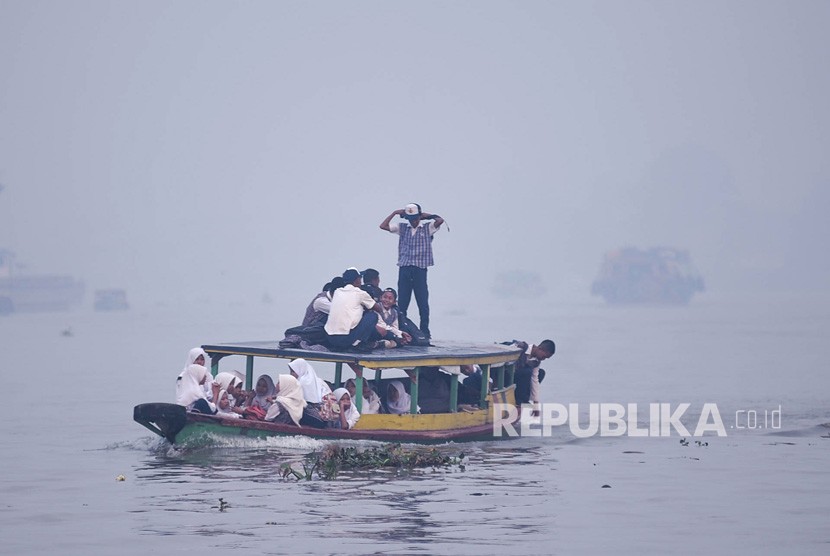 Sejumlah siswa menaiki kapal motor menembus kabut asap akibat kebakaran hutan dan lahan di Sungai Ogan, Palembang, Sumatera Selatan, Senin (16/9/2019).