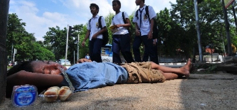 Sejumlah siswa SMP berjalan melintasi seorang anak gelandangan (putus sekolah) yang tertidur di kawasan Kebayoran Baru, Jakarta. 