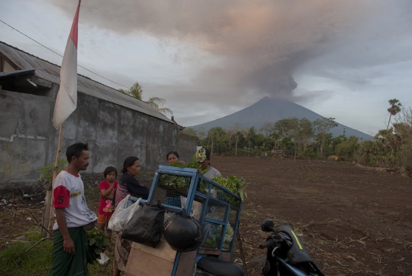 Sejumlah warga beraktivitas di sekitar rumahnya dengan latar belakang Gunung Agung meletus di Desa Datah yaitu desa yang termasuk dalam kawasan rawan bencana, Karangasem, Bali, Senin (27/11).