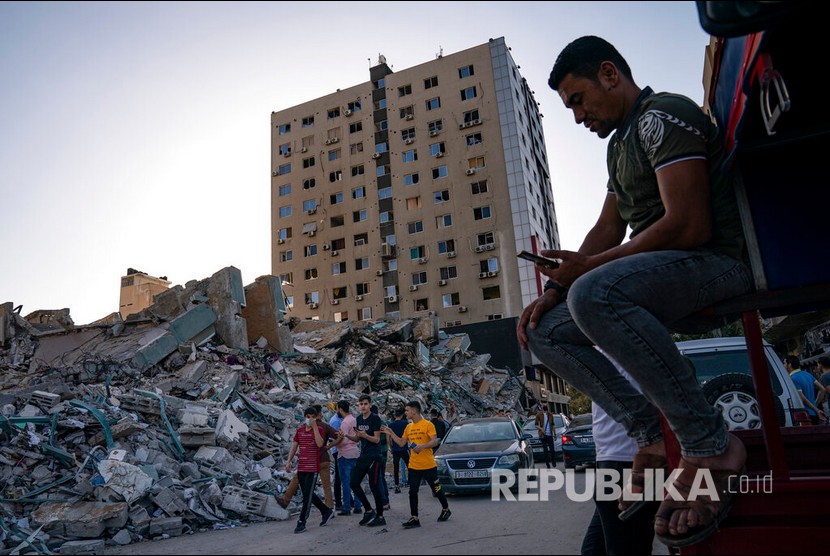 Sejumlah warga berjalan melewati reruntuhan gedung Al Jalaa yang hancur oleh serangan udara Israel, Gaza, Jumat (21/5) waktu setempat.  Sejumlah media internasional menempati gedung Al-Jalaa termasuk kantor berita Associated Press yang telah berkantor disana selama 15 tahun.