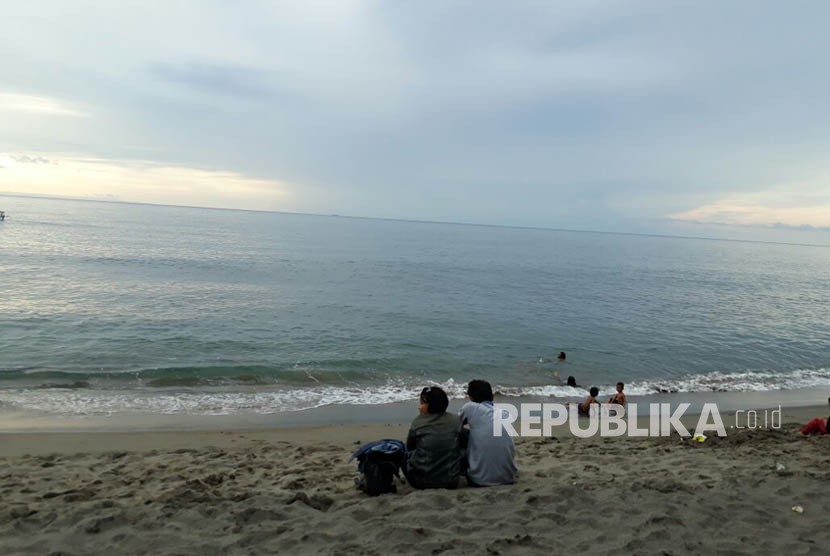 Sejumlah warga bermain air di Pantai Duduk, Kecamatan Batulayar, Kabupaten Lombok Barat, NTB pada Ahad (26/11) sore. Tampak dari kejauhan terlihat pemandangan Gunung Agung di Bali yang terlihat gelap.