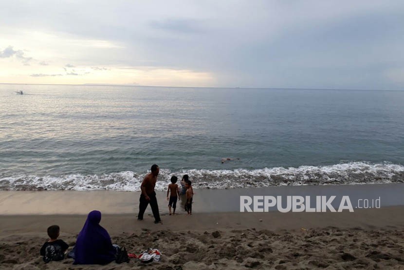 Sejumlah warga bermain air di Pantai Duduk, Kecamatan Batulayar, Kabupaten Lombok Barat, NTB pada Ahad (26/11) sore. Tampak dari kejauhan terlihat pemandangan Gunung Agung di Bali yang terlihat gelap.