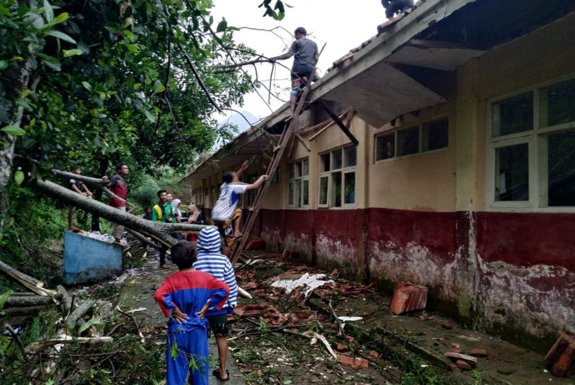 Sejumlah warga dan guru membersihkan sisa material pohon tumbang yang menimpa atas SDN 3 Cigorowong, Kampung Sukamaju, Desa Sukamukti, Kecamatan Cisayong, Kabupaten Tasikmalaya, Senin (3/2). Atap dua ruang kelas sekolah itu rusak akibat kejadian tersebut.