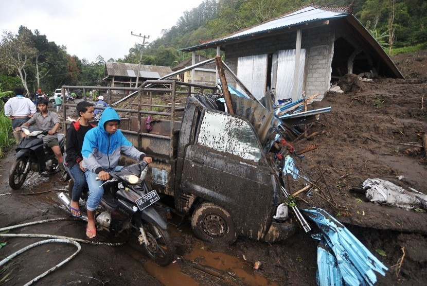 Sejumlah warga melintas di dekat rumah yang tersapu tanah longsor di Desa Songan, Kintamani, Bali, Jumat (10/2).