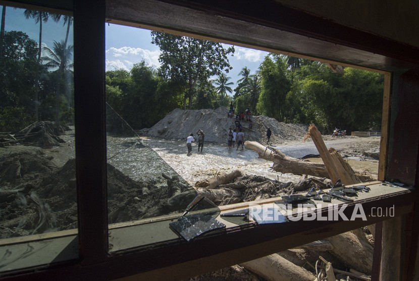 Sejumlah warga melintas di depan rumah yang tertimbun lumpur akibat banjir bandang di Desa Bangga, Sigi, Sulawesi Tengah. (Dok)