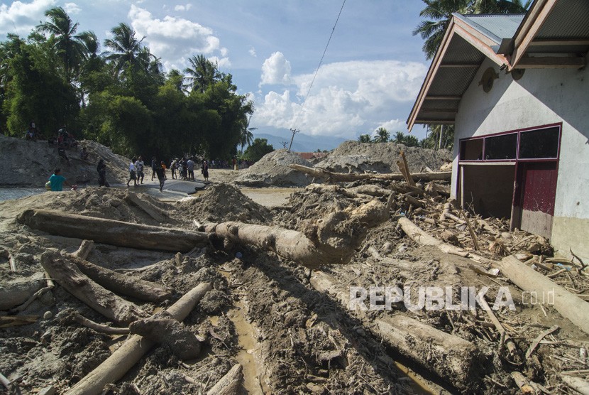 Sejumlah warga melintas di depan rumah yang tertimbun lumpur akibat banjir bandang di Desa Bangga, Sigi, Sulawesi Tengah, Jumat (23/11/2018).