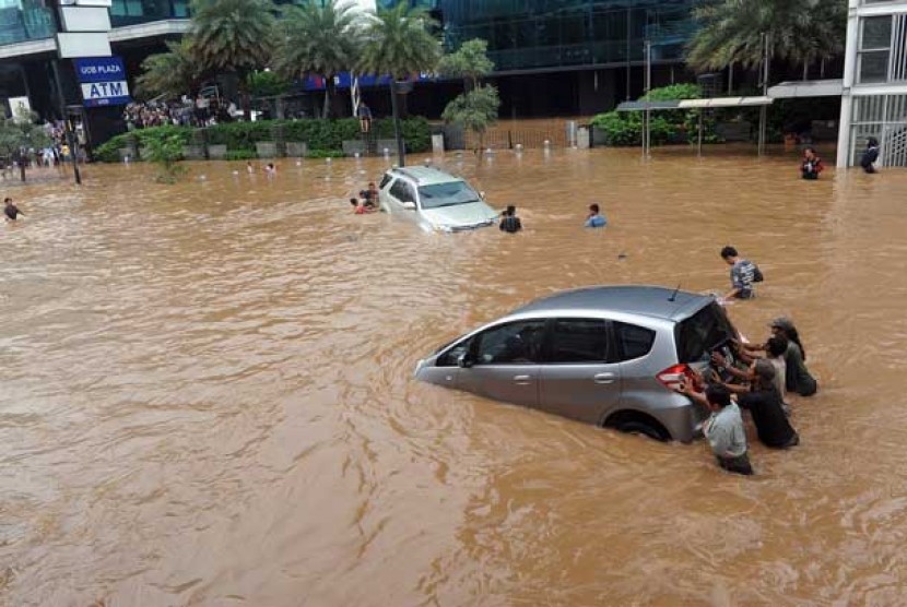 Sejumlah warga mendorong mobil yang terjebak banjir di kawasan Jl. Sudirman, Jakarta, Kamis (17/1).