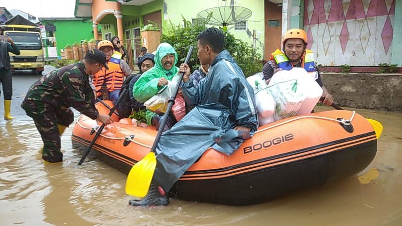 Sejumlah warga menggunakan perahu karet untuk melintasi jalan yang terendam banjir di Kabupaten Tasikmalaya. Polisi membantu korban banjir di Sukaresik, Tasikmalaya, Jawa Barat.