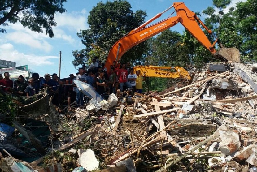 Sejumlah warga menyaksikkan proses evakuasi korban di salah satu bangunan yang runtuh akibat gempa 6.5 SR, di Desa Lueng Putu, perbatasan Pidie-Pidie Jaya, Aceh, Rabu (7/12). 