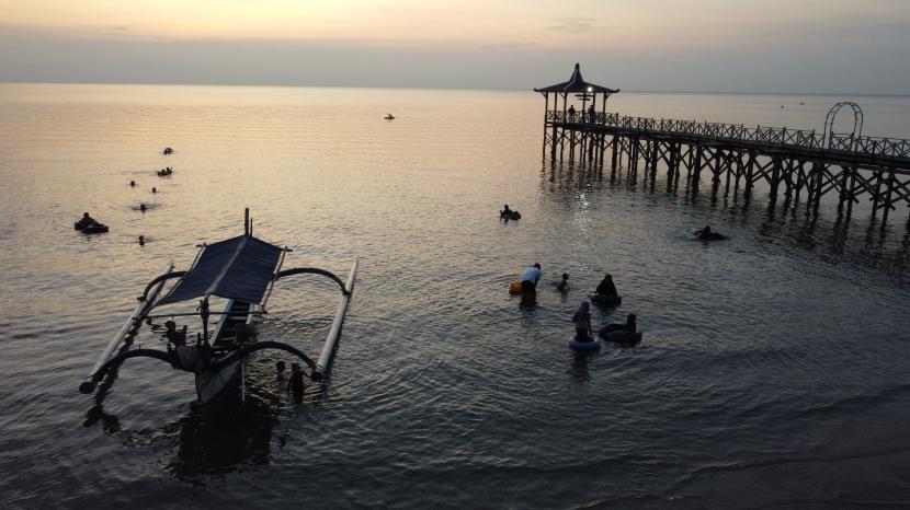 Sejumlah wisatawan bermain sambil menikmati suasana matahari tenggelam (Sunset) di Pantai Pasir Putih, Situbondo, Jawa Timur. Pengembangan infrastruktur marina penting untuk meningkatkan pariwisata bahari.