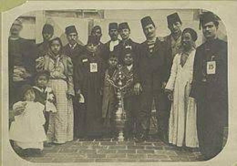Sekelompok imigran, sebagian besar mengenakan bulu halus, mengelilingi kapal besar yang dihiasi dengan simbol bintang dan bulan sabit Islam dan Turki Ottoman (1902–1913) 