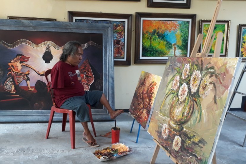 Seniman Kota Malang, Sadikin Pard melukis menggunakan kaki di Jalan Selat Sunda Raya D1/40B Kota Malang, Rabu (24/10). 