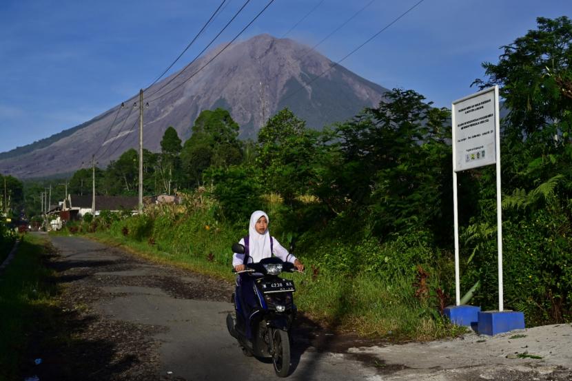 Seorang anak berangkat sekolah dengan latar belakang Gunung Semeru di Sumbermujur, Candipuro, Lumajang, Jawa Timur, Selasa (14/12/2021). Dinas Pendidikan Kabupaten Lumajang menyediakan tenda darurat untuk menggelar pendidikan karena sebagian sekolahan masih digunakan sebagai posko pengungsian dan logistik. 