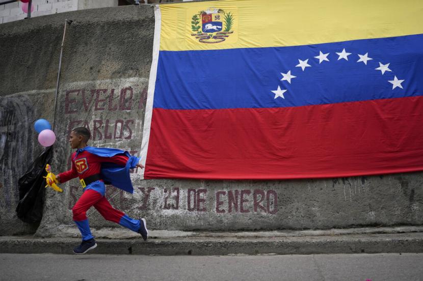 Seorang anak berlari melintasi bendera Venezuela, Senin (28/2/2022). Venezuela dan Amerika Serikat (AS) pada Sabtu (1/10/2022) saling bertukar tahanan. 