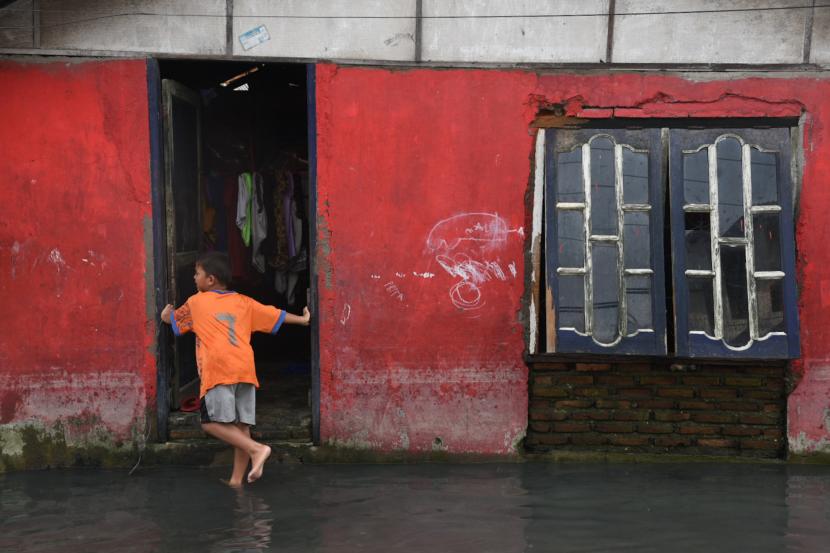 Seorang anak bermain di depan rumahnya yang terendam banjir rob. Ilustrasi.