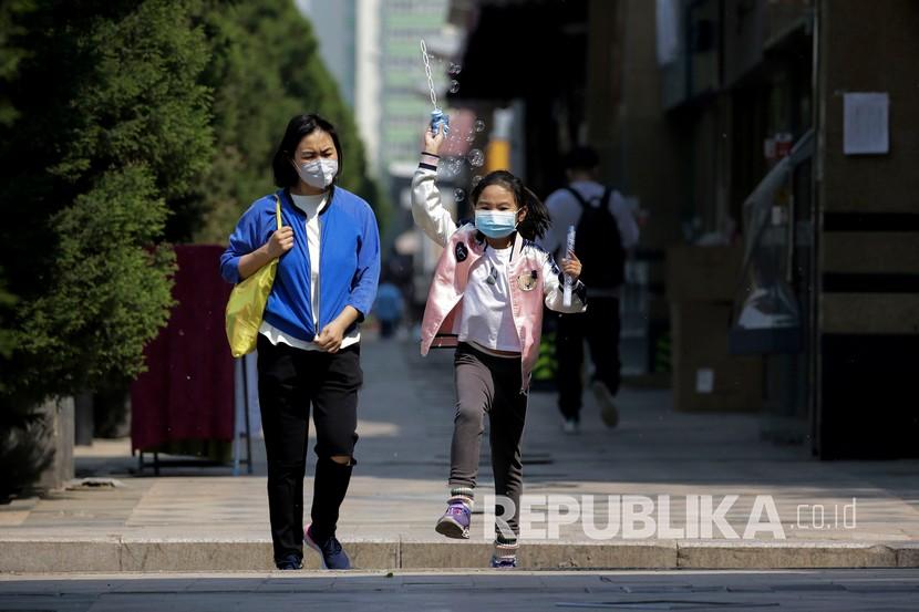 Seorang anak bersama wanita mengenakan masker saat melintasi trotoar di Beijing, Cina. ilustrasi
