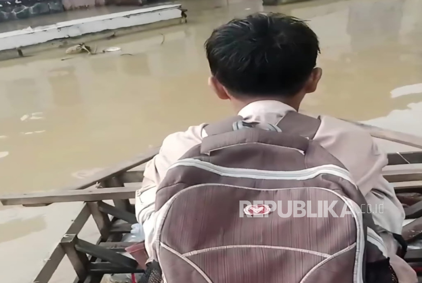 Seorang anak di Desa Eretan Wetan, Kecamatan Kandanghaur, Kabupaten Indramayu diantarkan ayahnya pergi ke sekolah menggunakan perahu rakit dari kayu dan galon bekas. Mereka menembus jalanan yang digenangi banjir rob, Kamis (20/11/2025). 