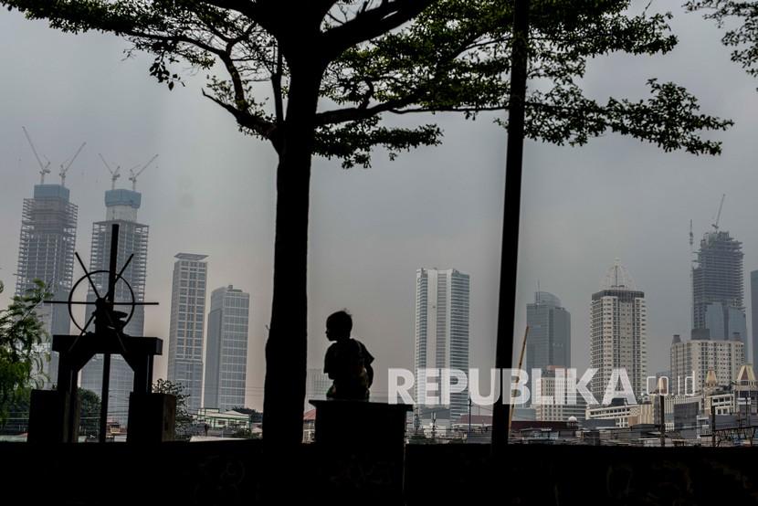 Seorang anak duduk di atas tanggul dengan latar belakang deretan bangunan gedung bertingkat di Jakarta, Rabu (27/10). Penerimaan pajak tercatat sebesar Rp 1.231,87 triliun per 26 Desember 2021.