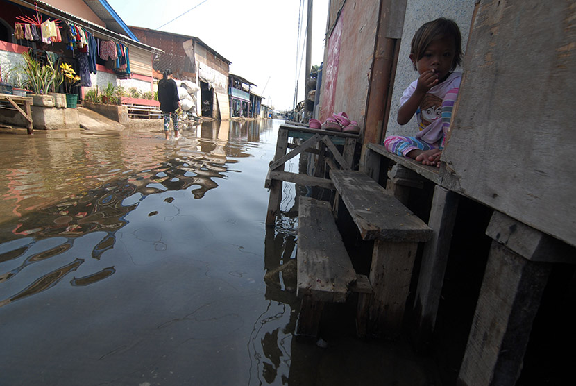 Seorang anak duduk di depan rumahnya yang terkena banjir rob (air laut pasang), di Dadap, Kabupaten Tangerang, Banten, Senin (23/11).