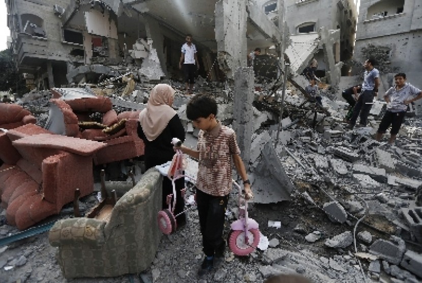 Seorang anak kecil berjalan di antara reruntuhan bangunan di Jalur Gaza yang dihantam roket militer Israel.