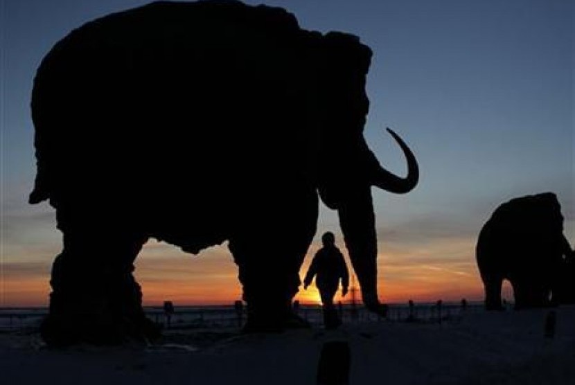 Seorang anak kecil berjalan melewati patung raksasa gajah purba atau mamut. 
