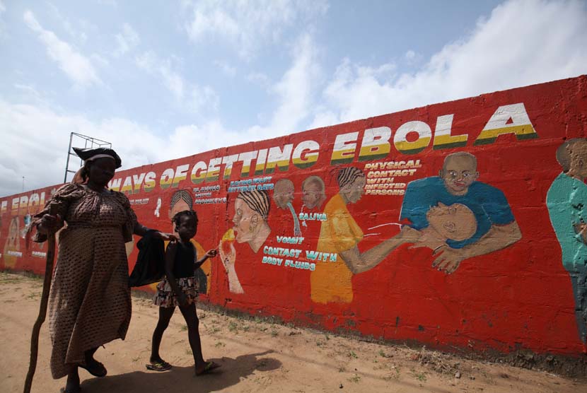 Seorang anak kecil bersama ibunya yang buta, berjalan melewati sebuah mural yang berisi pesan tentang ebola di Sinkor, Monrovia, Liberia, Agustus 2015. 