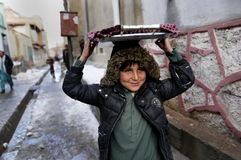 Seorang anak laki-laki membawa makanan di kepalanya di Kabul, Afghanistan, Selasa (8/2/2022).