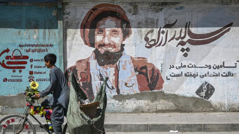 Seorang anak laki-laki menjajakan melewati lukisan dinding dengan potret mendiang komandan Afghanistan Ahmad Shah Massoud di Kabul pada 8 September 2021.