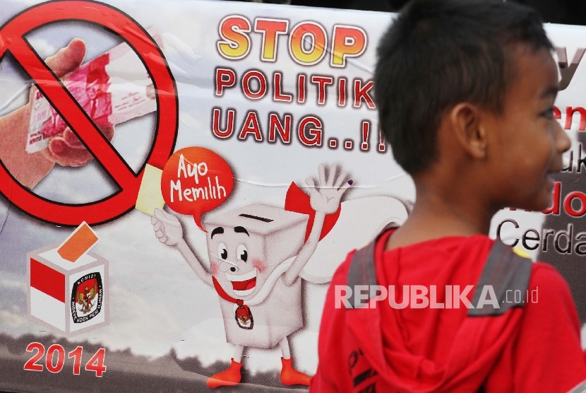 Seorang anak melintas di depan poster Stop Politik Uang.  (ilustrasi)