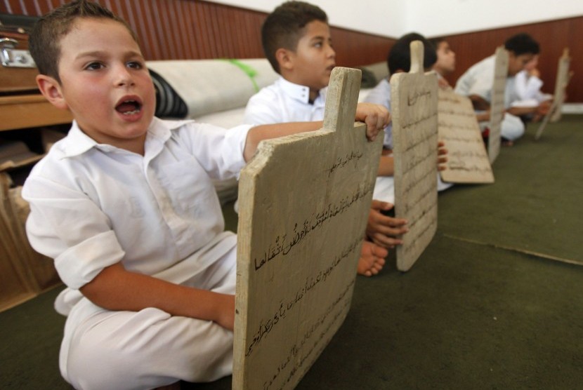 Seorang anak membaca sebuah papan tulis kayu sambil menghafal Alquran di Tripoli, Libya, Senin (23/7).   (Ismail Zitouny/Reuters)