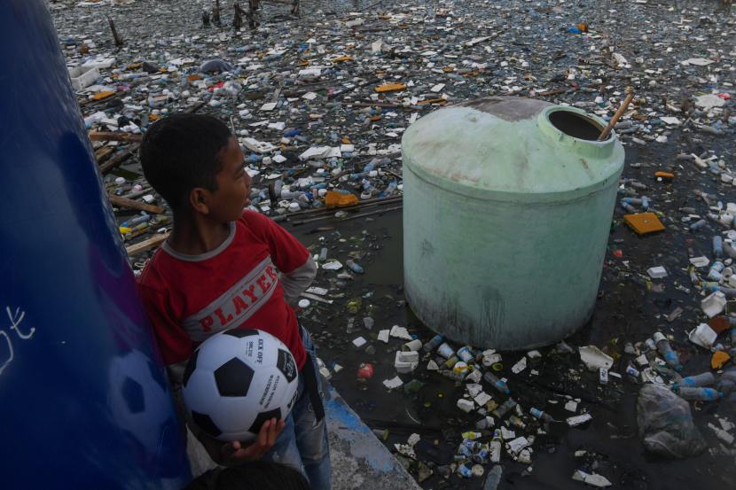 Seorang anak memegang bola sambil melihat hamparan sampah plastik yang terapung di Muara Angke, Jakarta Utara, Senin (4/7/2022). Badan Pusat Statistik akan mendata jumlah penduduk miskin ekstrem sebagai acuan dalam program percepatan penghapusan kemiskinan ekstrem yang ditargetkan dapat tercapai pada tahun 2024. 