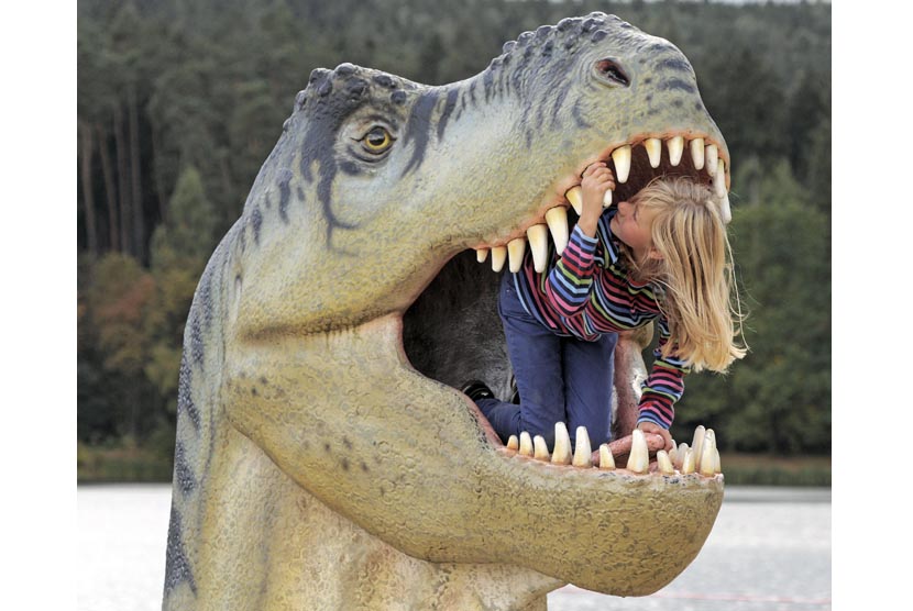 Seorang anak bermain di dalam mulut patung dinosaurus.  
