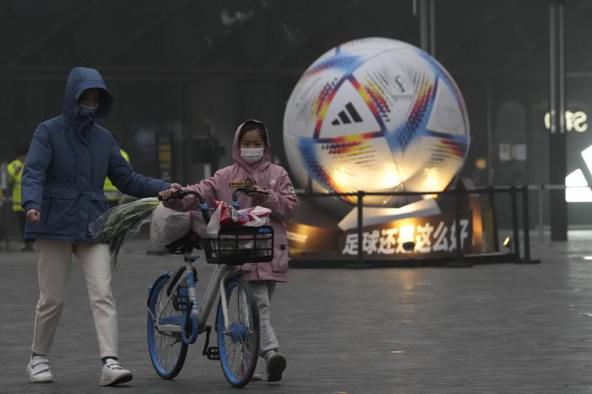  Seorang anak mendorong sepeda dengan bahan makanan melewati replika sepak bola raksasa yang ditempatkan untuk mempromosikan Piala Dunia FIFA Qatar di Beijing, Ahad, 20 November 2022. 