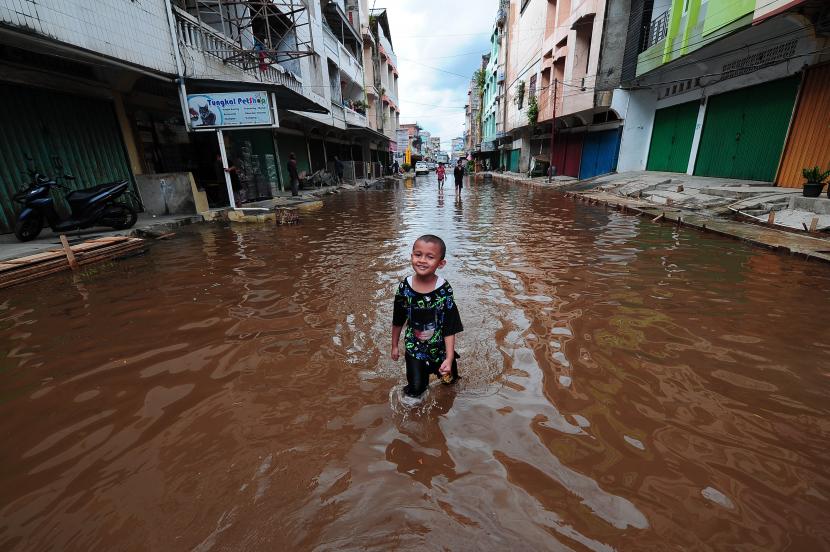 Seorang anak menerobos jalan saat banjir rob menggenangi kawasan pertokoan Kuala Tungkal, Tanjungjabung Barat, Jambi, Sabtu (4/12/2021). Kuala Tungkal yang berada di pesisir timur Provinsi Jambi mengalami bajir rob musiman hingga menggenangi kawasan pertokoan setempat. 