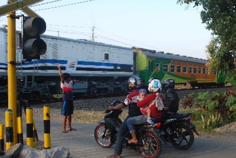 Seorang anak mengatur lalu lintas ketika ada kereta yang melintas di sebuah perlintasan kereta api. 