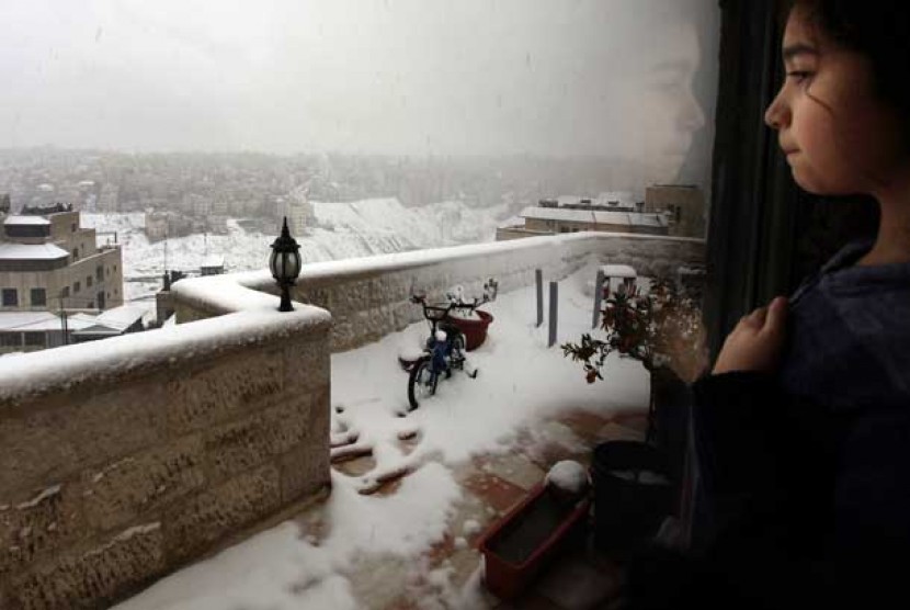   Seorang anak menyaksikan hujan salju dari jendela kamar tidurnya, di Amman, Yordania, Kamis (10/1).