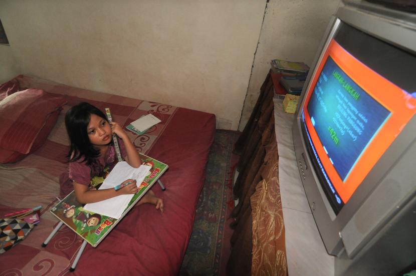 Seorang anak menyimak pembelajaran yang disiarkan melalui televisi. 