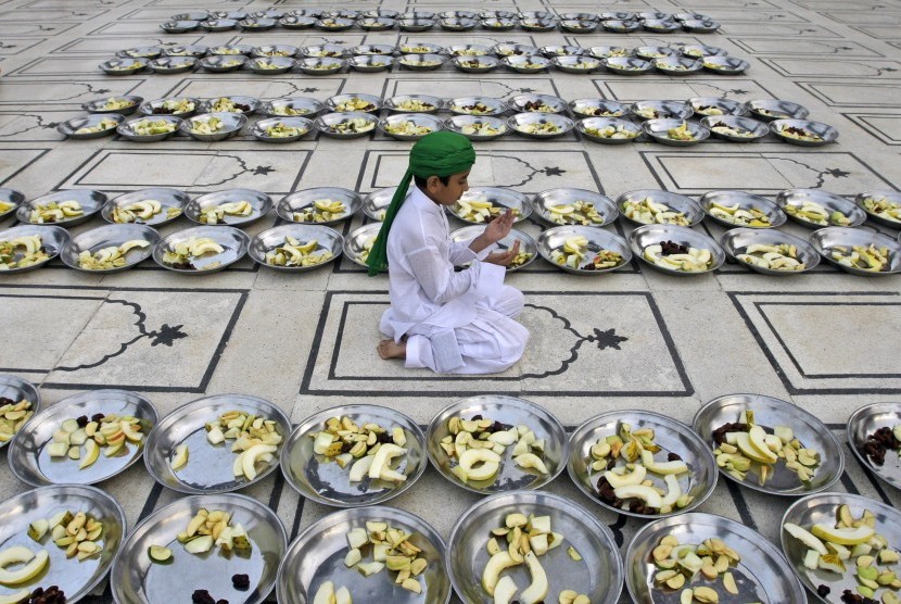   Seorang anak Pakistan berdoa diantara deretan piring berisi buah yang disumbangkan untuk jamaah yang hendak berbuka puasa di sebuah masjid di Karachi, Pakistan, Sabtu (21/7).  (Shakil Adil/AP)