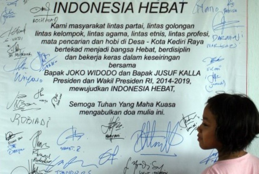Seorang anak perempuan melihat spanduk yang berisi dukungan elemen masyarakat dan tanda tangan dukungan pasangan capres Jokowi-JK di Kediri, Jawa Timur, Ahad (15/6). 