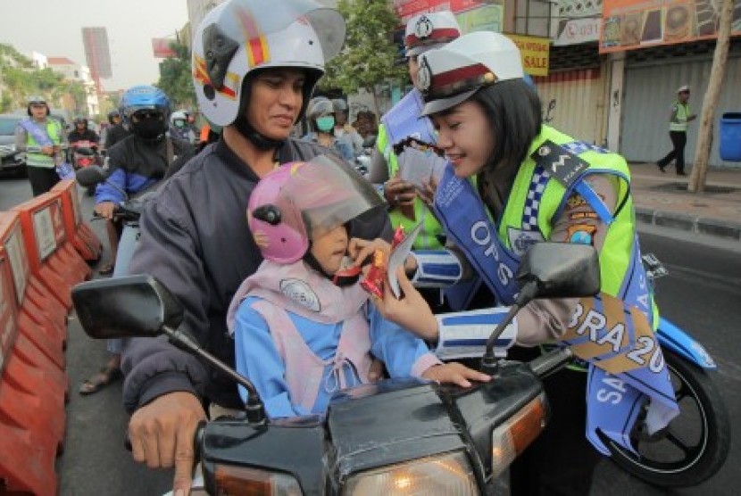 Seorang anggota kepolisian memasangkan pengikat helm pengendara motor yang tidak terpasang di Surabaya, Jawa Timur, Selasa (27/10). 