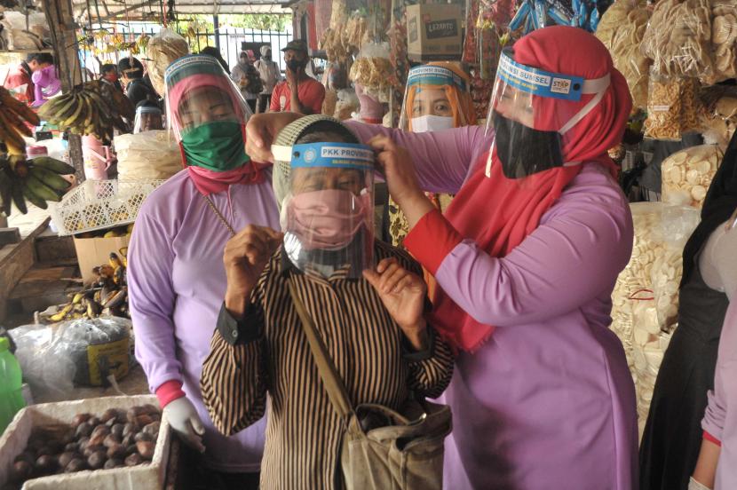 Seorang anggota PKK memakaikan pelindung wajah (face shield) kepada salah satu pedagang pada sosialisasi alat pelindung diri (APD) bagi pedagang di Pasar Sekip Ujung, Palembang, Sumatera Selatan.