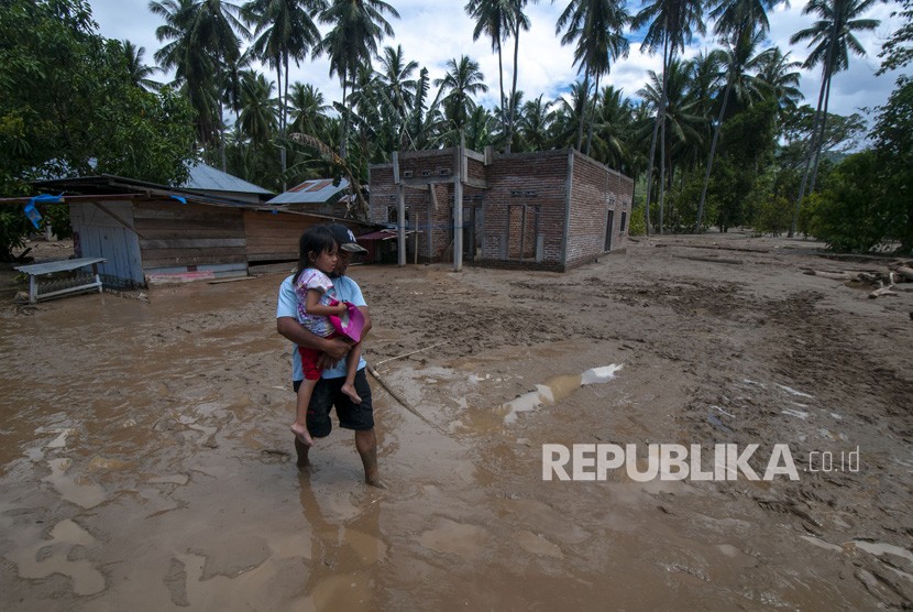 Seorang bapak menggendong anaknya melitnsi lumpur di dekat rumahnya pada banjir bandang di Desa Bangga, Dolo Selatan, Sigi, Sulawesi Tengah, Senin (29/4/2019). 