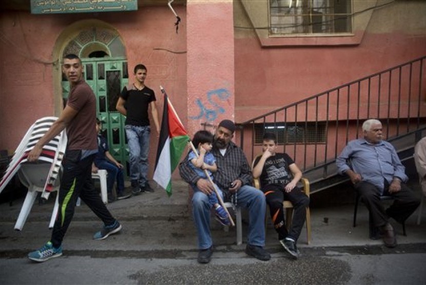Seorang bocah laki-laki Palestina memegang bendera Palestina sambil duduk di pangkuan ayahnya.