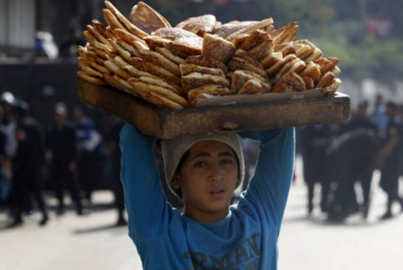 Seorang bocah lelaki membawa roti di atas kepala berjalan menjauh dari kerumunan rusuh di Lapangan Tahrir, Kairo.