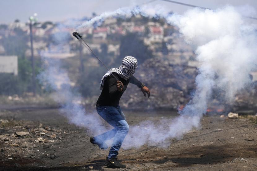 Seorang demonstran Palestina melemparkan kembali tabung gas air mata yang ditembakkan oleh pasukan Israel selama protes terhadap permukiman Yahudi Tepi Barat, di desa Kafr Qaddum Tepi Barat, Jumat, 20 Mei 2022.